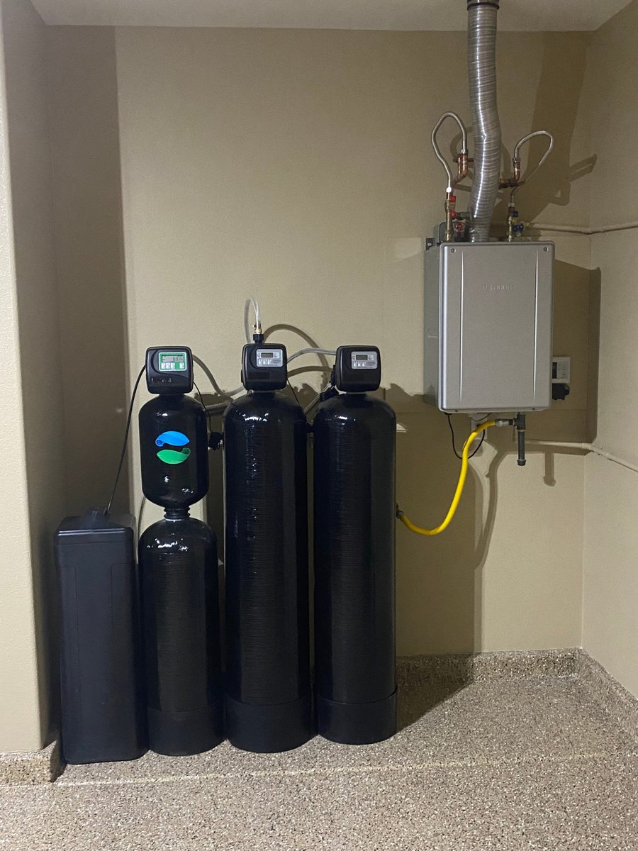 Noritz tankless water heater mounted on the wall beside three water refinement tanks on an epoxy floor